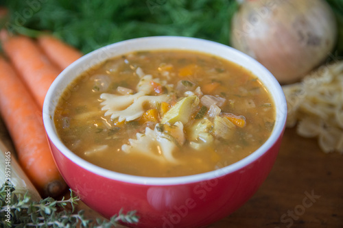 Minestrone soup, a typical thick vegetables soup, originally from Italy, served in a red bowl with Farfalle Pasta. 