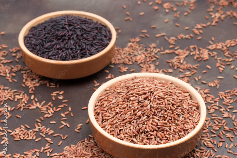 Red brown rice in ceramic bowl. Black brown rice in ceramic bowl. Rice is scattered on table Red brown rice in ceramic bowl. Black brown rice in ceramic bowl. Rice is scattered on table