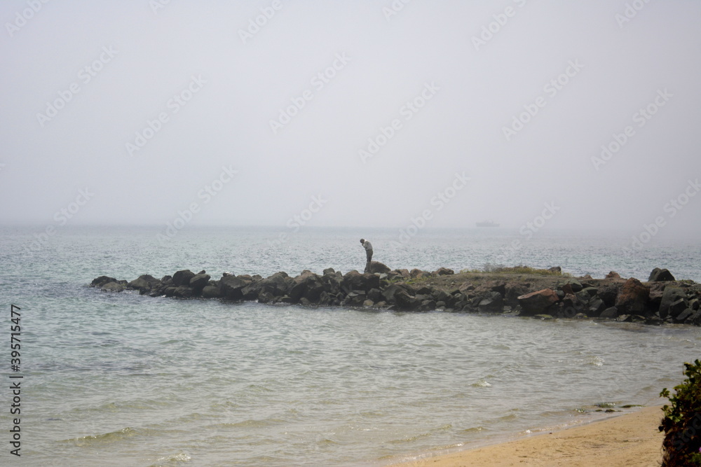 Ravda, Bulgaria. May, 20, 2014. Stone breakwater watercutter with sulouette of fisherman in misty weather, calm water and sandy beach