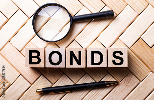 Wooden cubes with the word BONDS stand on a wooden background between a magnifying glass and a handle