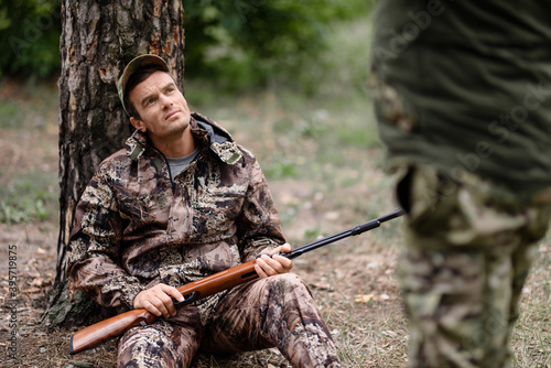 Hunter with Rifle Has Rest Men Hunting in Forest.