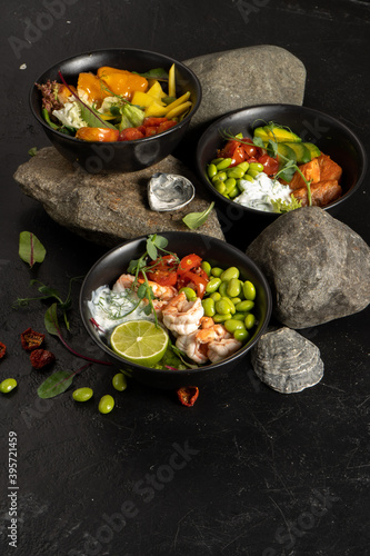 Three black ceramic bowls with assorted vegetarian Asian dishes of fish, shrimp, seafood, beans and avocado with yogurt dressing, lettuce and herbs.