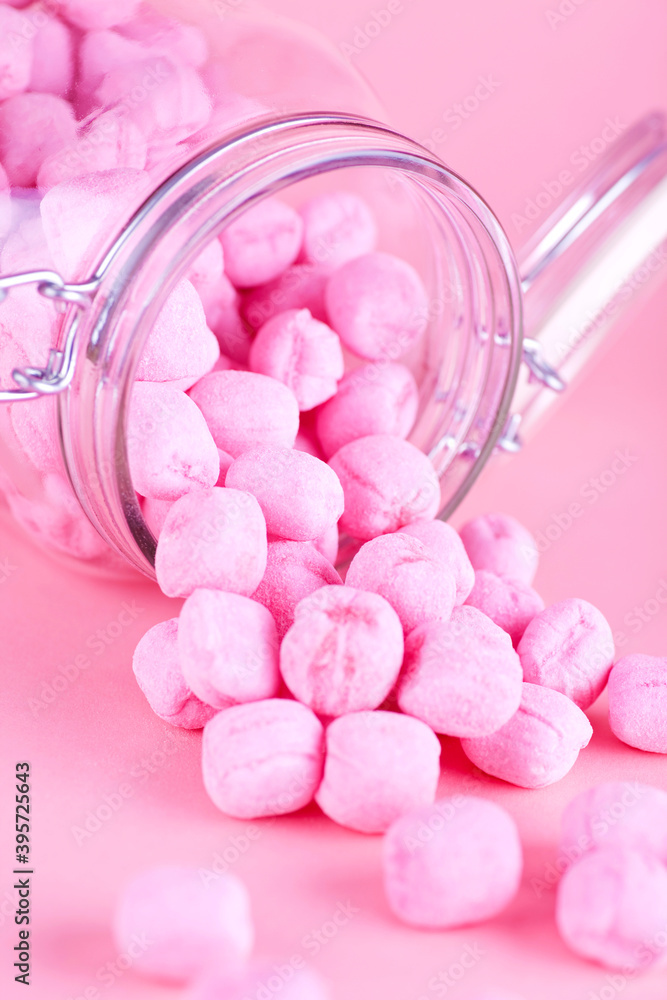 Glass jar filled with pink candy. Studio photo isolated on pink background. Selective focus on object. Glass jar filled with pink candy. Studio photo isolated on pink background. Selective focus on object.
