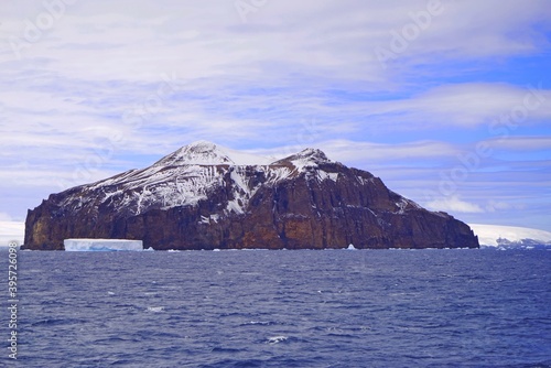 There is a rocky mountain in the sea, the top of which is covered with some snow. There is a small iceberg in front of it.