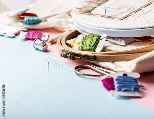 Embroidery set fot cross stitching. White fabric, embroidery hoop, colorful threads, scissors and needls. On blue background. Hobbies concept with copy space. photo