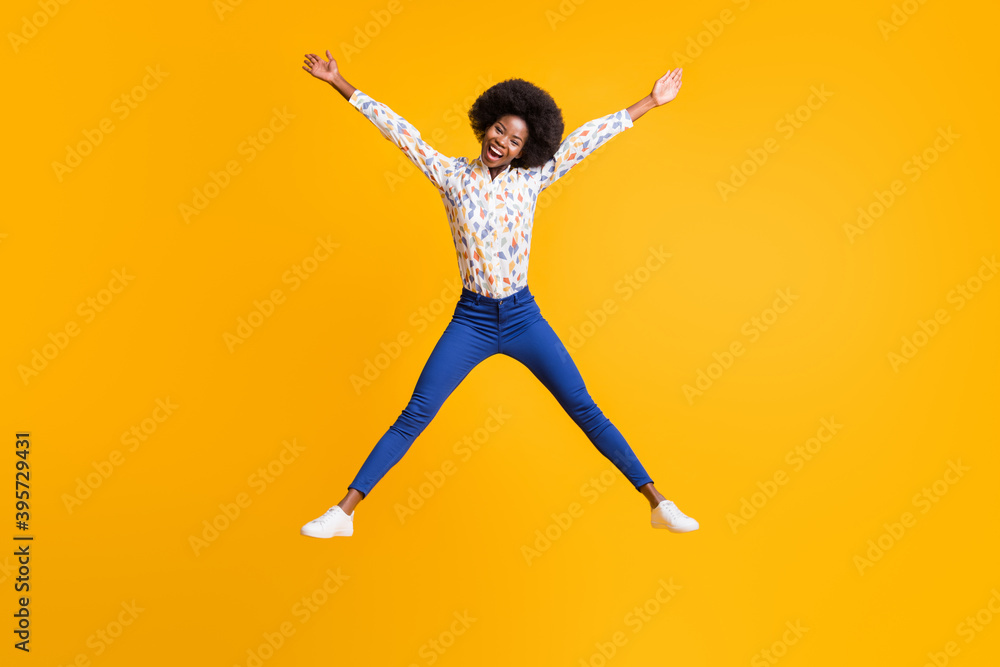 Full length photo of carefree funny dark skin woman wear casual outfit jumping legs arms sides isolated yellow color background