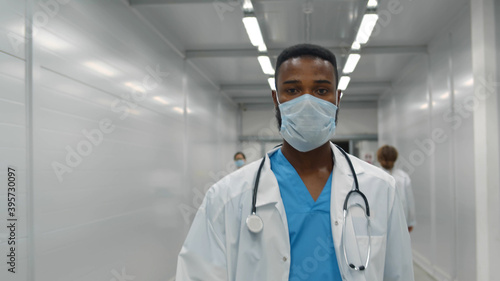 Portrait of afro doctor man wearing protective mask walking in hospital hall