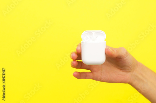 Female hand holding a case with headphones on a yellow background