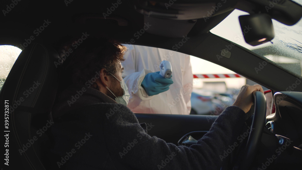 Person in a protective suit checking temperature of male driver