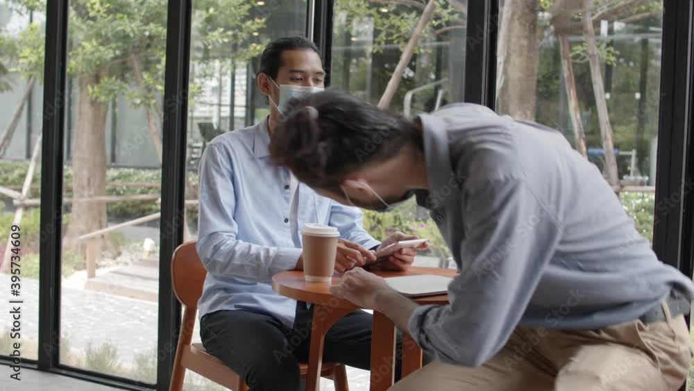 Asian businessmen wearing mask and greeting with elbow and talking with big smiled, discussing about success business, drinking coffee in café working space Asian businessmen wearing mask and greeting with elbow and talking with big smiled, discussing about success business, drinking coffee in café working space