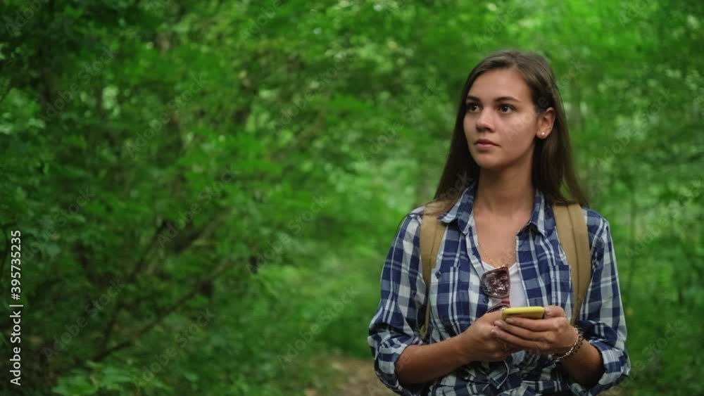 Young female is walking in wood, holding cellphone Young female is walking in wood, holding cellphone