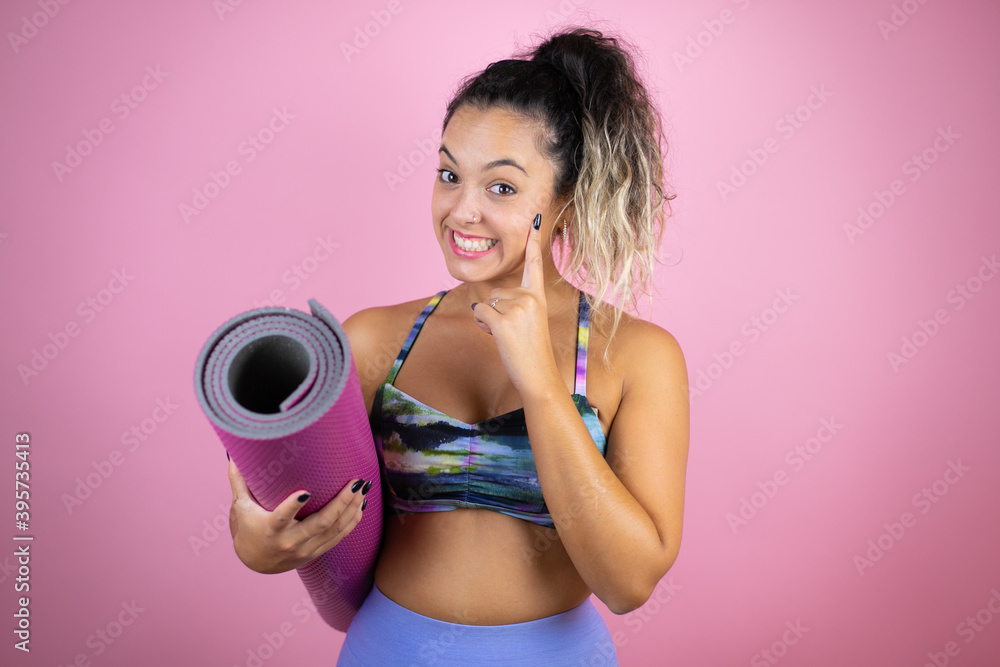 Young beautiful woman wearing sportswear and holding a splinter over isolated pink background smiling confident showing and pointing with fingers teeth and mouth Young beautiful woman wearing sportswear and holding a splinter over isolated pink background smiling confident showing and pointing with fingers teeth and mouth