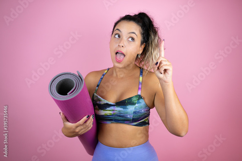 Young beautiful woman wearing sportswear and holding a splinter over isolated pink background surprised, pointing and looking up.