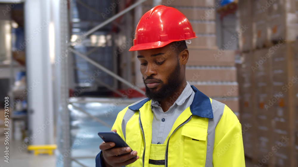African worker using smartphone standing in large industrial warehouse African worker using smartphone standing in large industrial warehouse