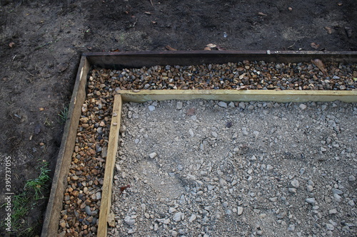 Close up of shed base construction of wood edging prepared hardcore mortar concrete flint brick compressed surface , a gravel surround french drain & brown earth soil & garden fencing background photo