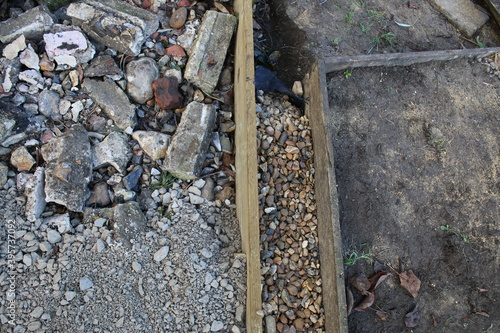 Close up of shed base construction of wood edging prepared hardcore mortar concrete flint brick compressed surface , a gravel surround french drain & brown earth soil & garden fencing background photo