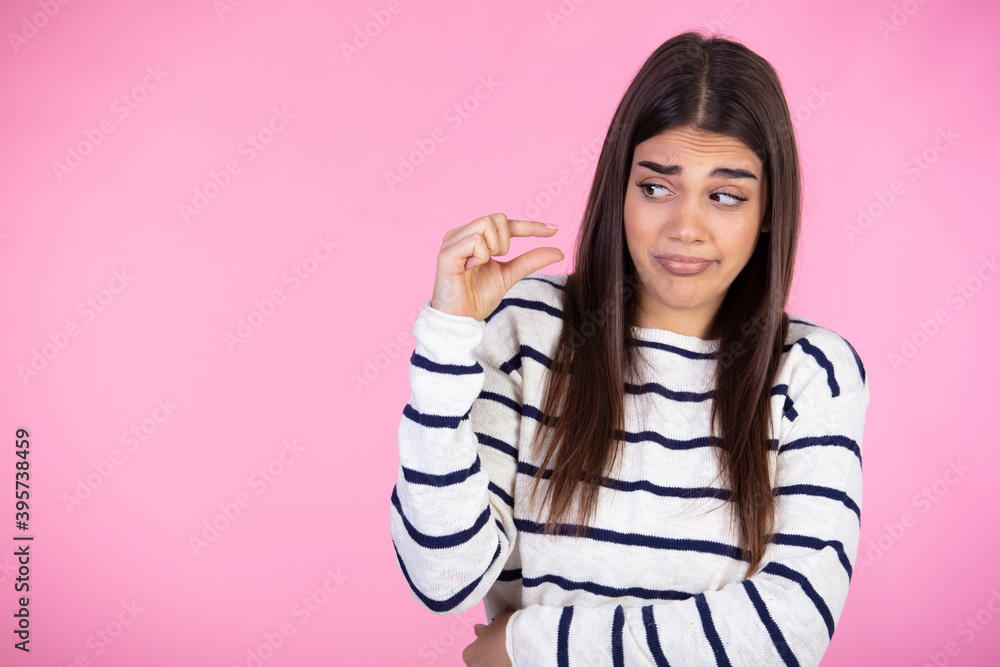 Half length portrait of woman showing small amount of something and having sneering facial expression, posing isolated over rosy background, good looking lady wearing striped sweater. People concept. Half length portrait of woman showing small amount of something and having sneering facial expression, posing isolated over rosy background, good looking lady wearing striped sweater. People concept.