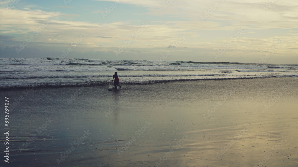 Kids playing football on the beach, wave on the background