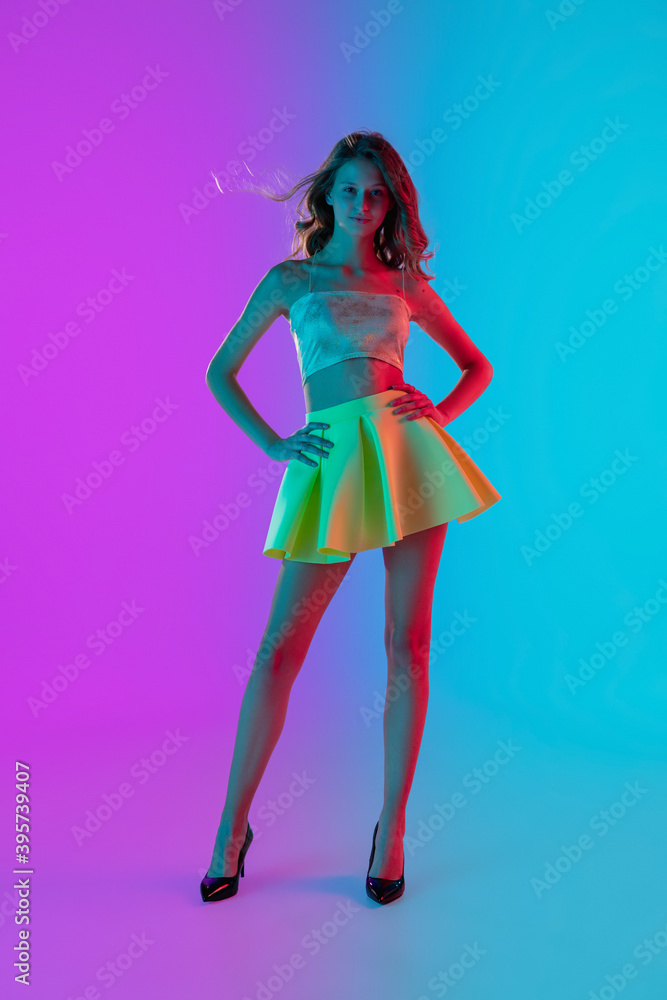 Fototapeta Model posing. Beautiful seductive girl in fashionable yellow skirt on gradient pink-blue neon background. Full-length portrait. Copyspace for ad. Flyer design. Summer, fashion, emotions concept.