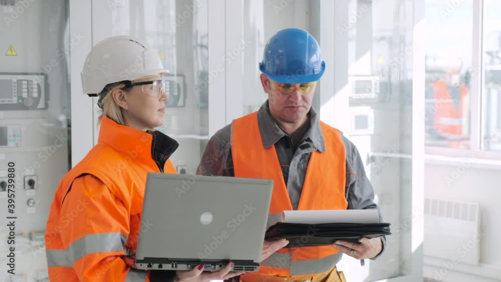 Team of employees in uniform with laptop and papers do pre-commissioning works checking wind power plant electrical station Team of employees in uniform with laptop and papers do pre-commissioning works checking wind power plant electrical station