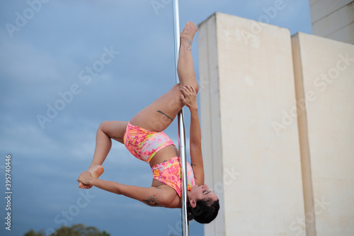 Young Middle Eastern pole dancer, holding a pose on a pole set in an urban park.