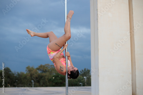 Young Middle Eastern pole dancer, holding a pose on a pole set in an urban park.