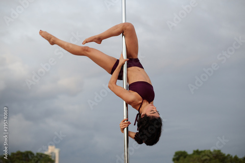 Young Middle Eastern pole dancer, holding a pose on a pole set in an urban park.