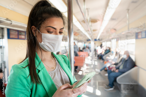 Woman with facial mask using cellphone on the train. Person standing looking at screen of mobile device while making transportation around the city.
