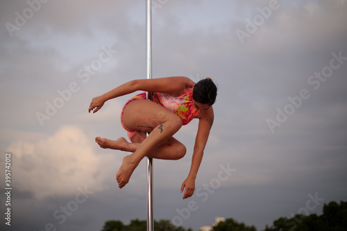 Young Middle Eastern pole dancer, holding a pose on a pole set in an urban park.
