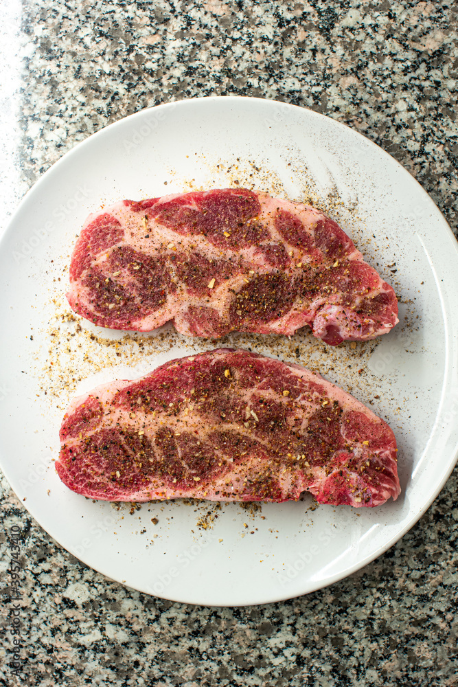 Obraz premium Fresh raw seasoned pork steak meat slices set on white porcelain dish on kitchen table