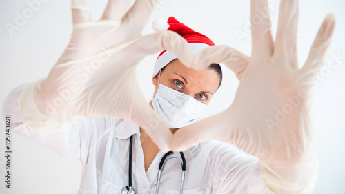 Woman doctor with a medical mask and hands in latex glove shows the symbol of the heart during the Christmas and New Year holidays.