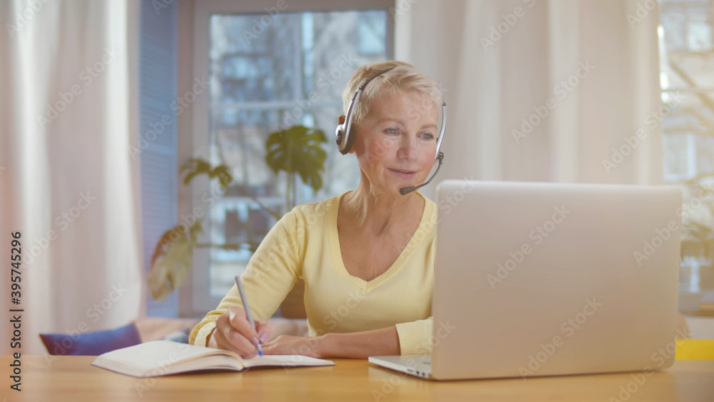 Mature woman with headset and laptop computer having video conference at home office