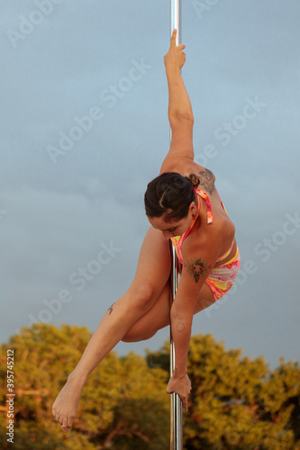 Young Middle Eastern pole dancer, holding a pose on a pole set in an urban park.