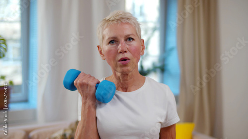 Close-up portrait of exhausted elderly woman doing exercises with dumbbells at home