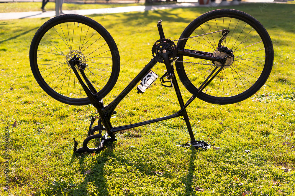 an inverted bike stands in the park with its wheels upside down