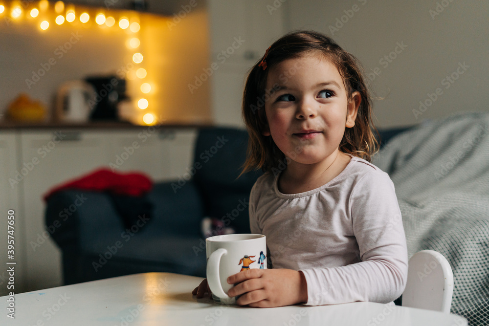 Caucasian toddler girl drinking cocoa from mug at home. Christmas bokeh lights Caucasian toddler girl drinking cocoa from mug at home. Christmas bokeh lights