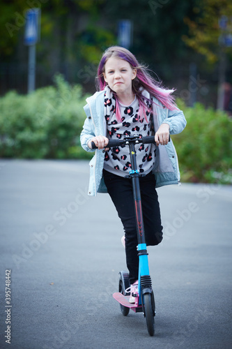 Happy beautiful girl is riding along the street on the kick scooter on a windy day. Baby having free time playing. The concept of a healthy lifestyle. Kids sport