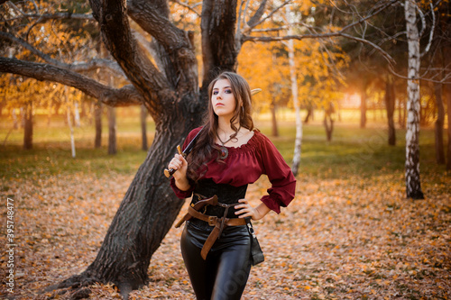 Portrait of an attractive slender woman with a saber on her shoulder against the background of an autumn park.