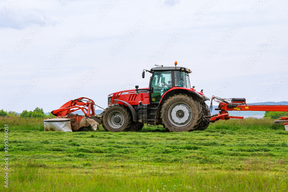 A big red tractor mows the grass for silage on the field A big red tractor mows the grass for silage on the field