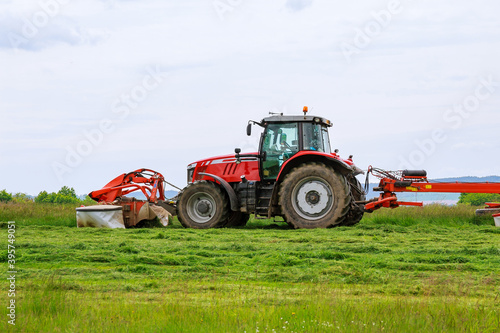 A big red tractor mows the grass for silage on the field