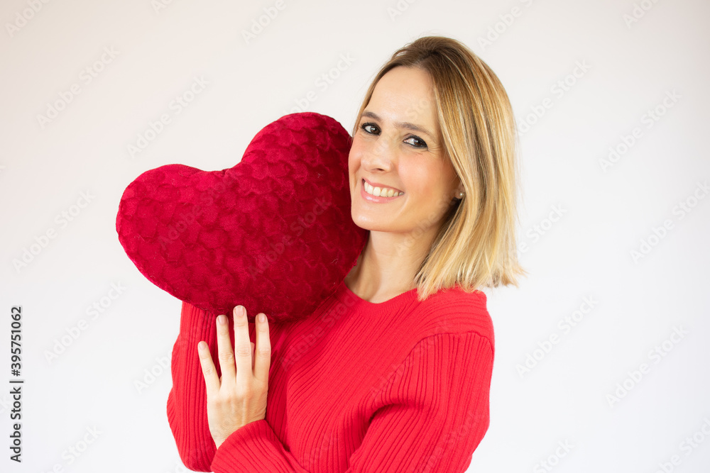 Happy young woman holding a red heart cushion over red background Happy young woman holding a red heart cushion over red background