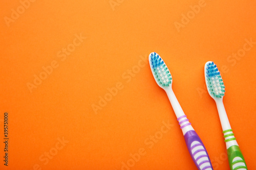 Two toothbrushes on orange background with copy space.