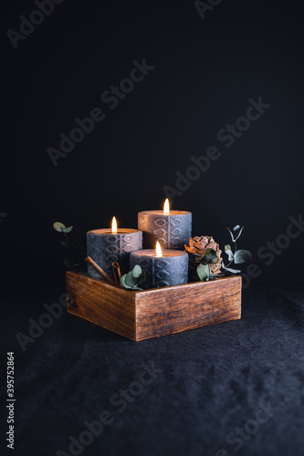 New Year festive decorations with wooden box and black burning candles in a dark interior.