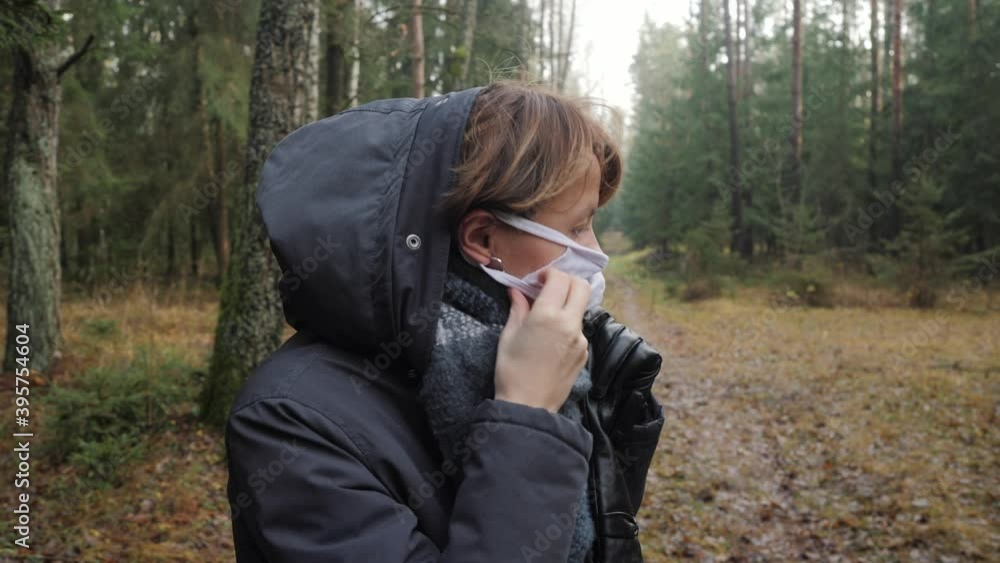 A girl in warm clothes puts on a protective mask in the forest. A girl in warm clothes puts on a protective mask in the forest.