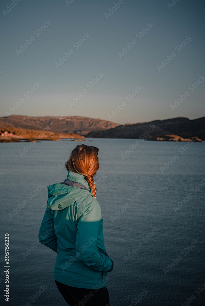 Young woman is enjoying beautiful view of sunset over norwegian fjord