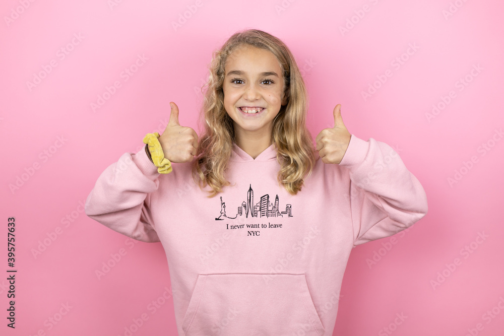 Young beautiful child girl standing over isolated pink background smiling confident doing the ok signal with her thumbs Young beautiful child girl standing over isolated pink background smiling confident doing the ok signal with her thumbs