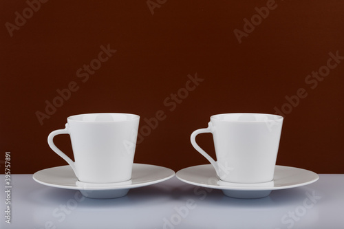 Two coffee cups on white table against brown background