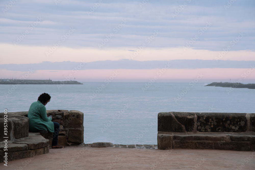 Mujer viendo el móvil sentada al bordo del mar en Hondarribia