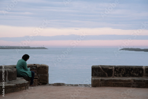 Mujer viendo el móvil sentada al bordo del mar en Hondarribia © Safi