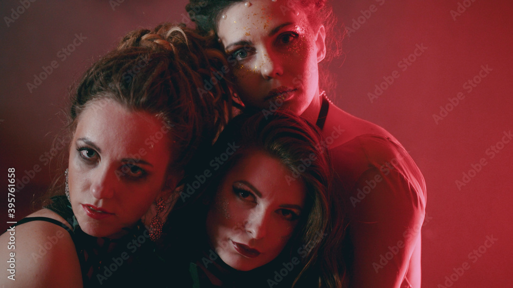 Portrait of beautiful three women with stylish sparkling makeup hugging and looking at camera